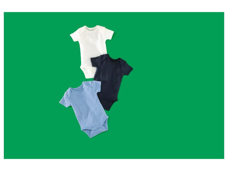 Drie babyrompertjes in wit, marineblauw en lichtblauw, diagonaal gerangschikt op een groene achtergrond.