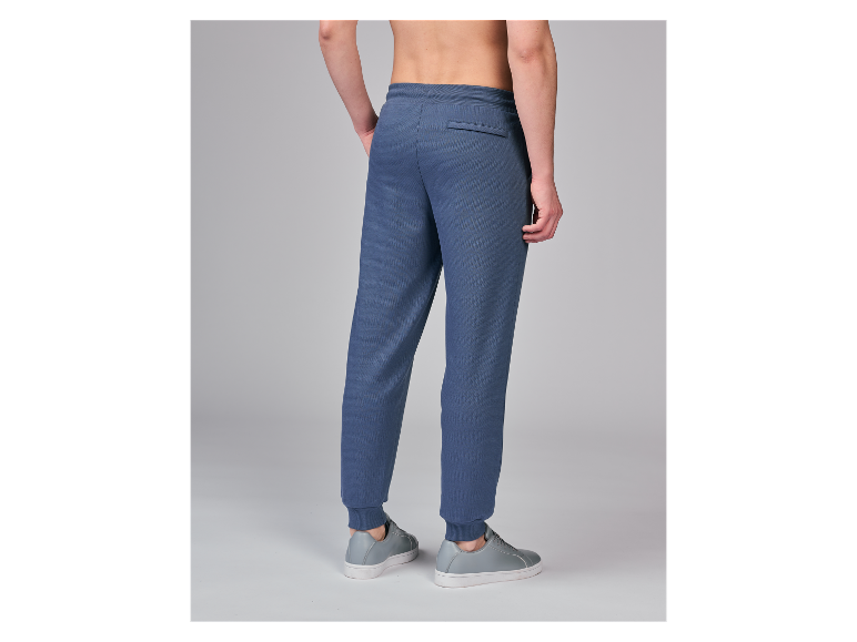 Man van achteren gezien met blauwe joggingbroek en grijze sneakers.