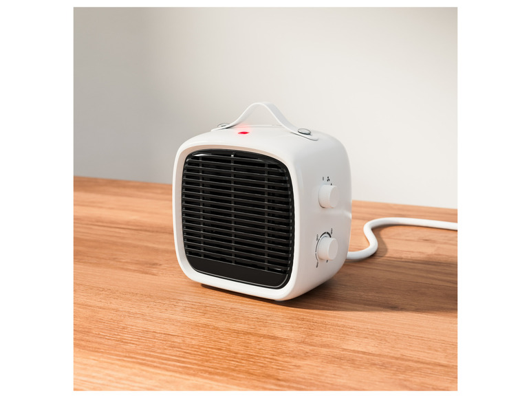 Een wit elektrische kacheltje met een handvat op een houten tafel.