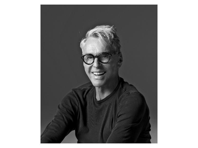 Zwart-wit portret van een lachende man met grijs haar en bril.