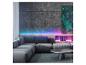 Moderne woonkamer met grijze hoekbank, ronde salontafel en kleurrijke LED-verlichting.