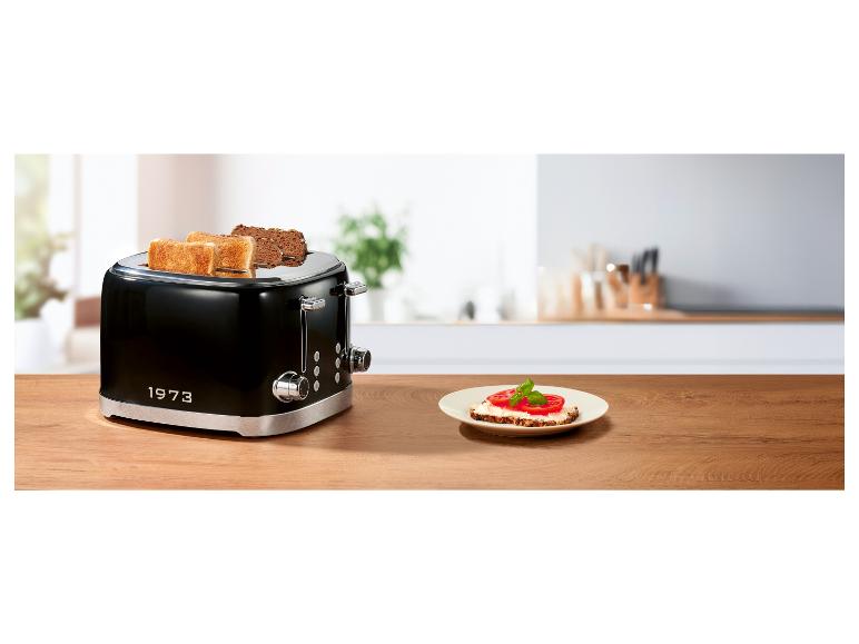 Zwarte broodrooster met toast en een bord met tomatenbrood op een houten tafel.