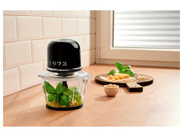 Zwarte hakmolen met pesto-ingrediënten op houten plank in de keuken.
