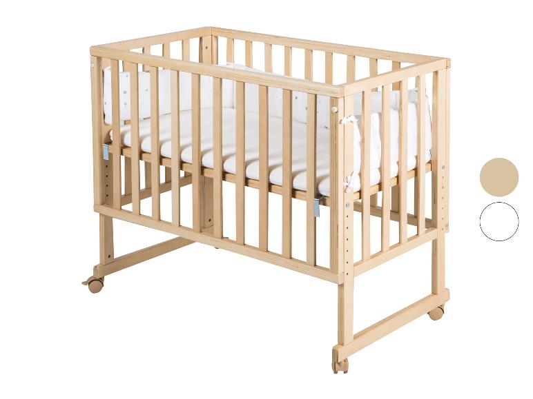 Licht houten babybedje met wit beddengoed en wieltjes.