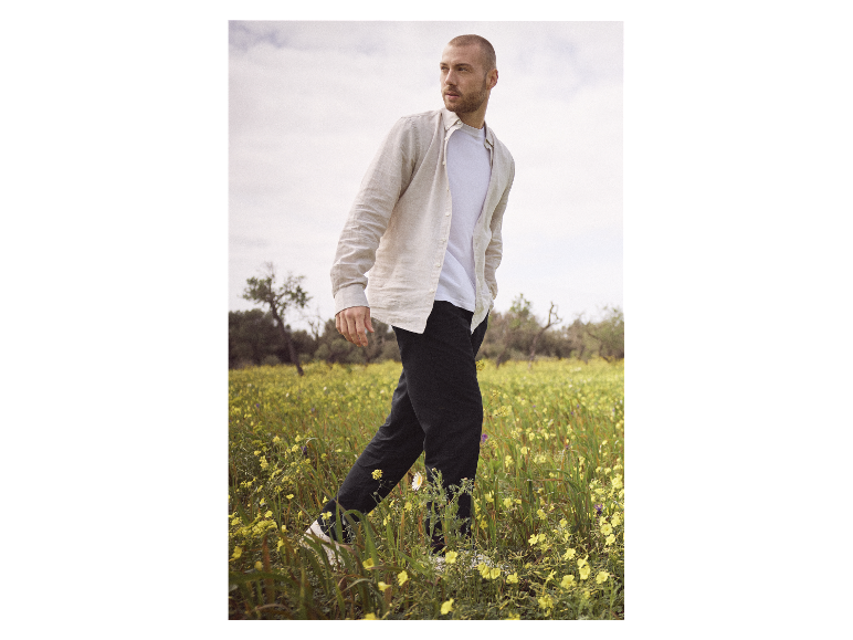 Man loopt door een bloemenveld, draagt een linnen overhemd en broek.