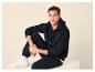 Man in donkerblauwe hoodie en joggingbroek, zittend met witte sneakers.