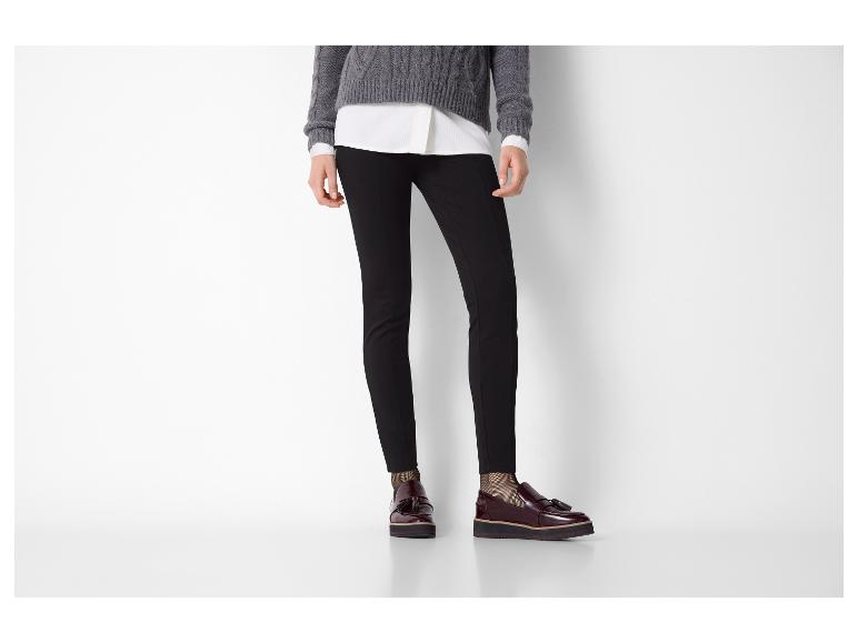 Vrouw in grijze trui, wit overhemd, zwarte broek en bordeauxrode loafers.