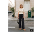 Vrouw in beige gebreid T-shirt, zwarte broek met wijde pijpen en sleehakken.