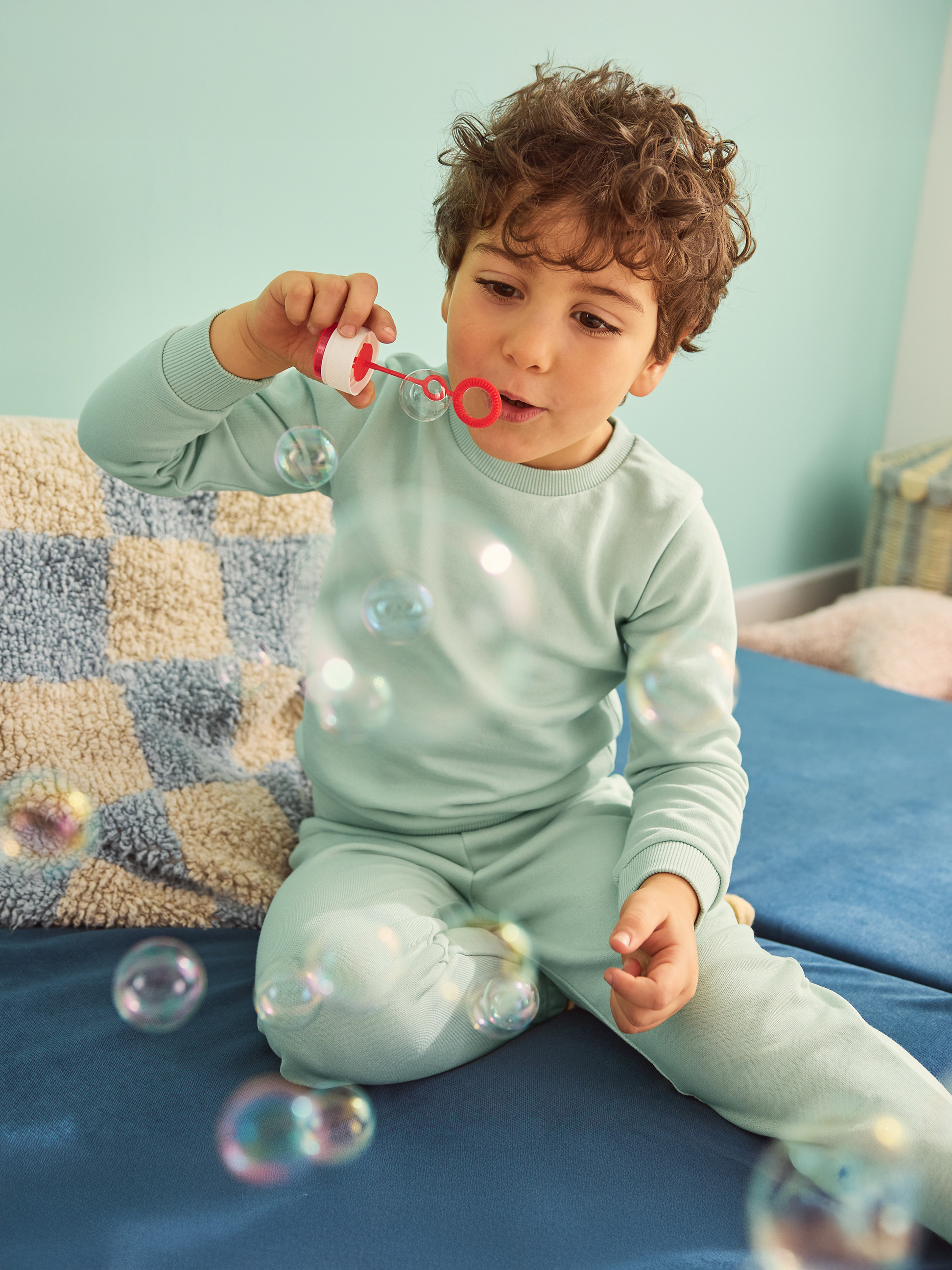 Jongen in blauwe pyjama blaast bellen op een blauwe bank.