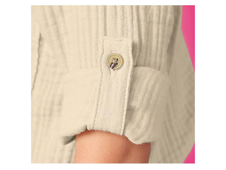 Close-up van een beige linnen overhemdsmouw met opgerolde manchet en knoop