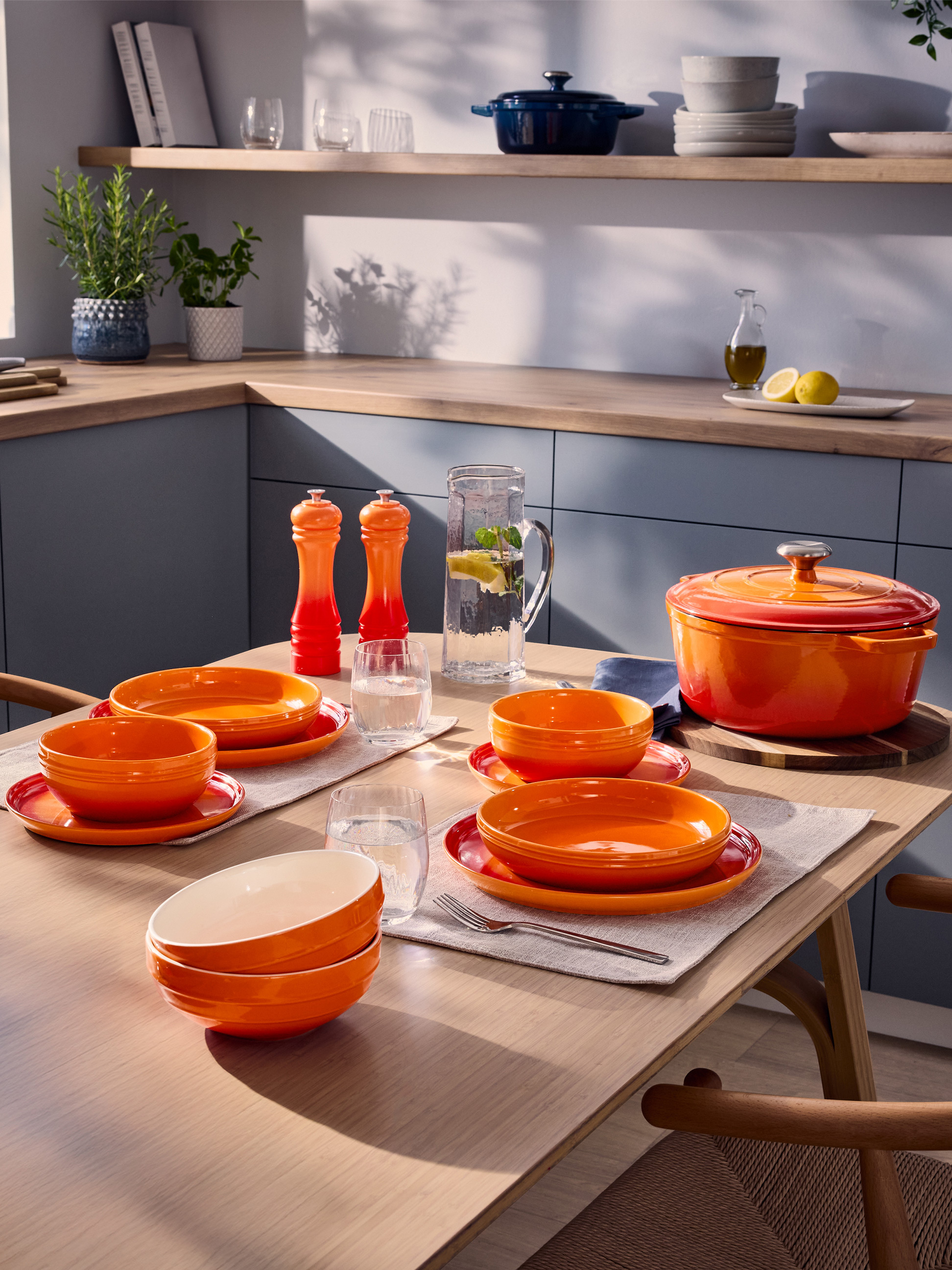 Oranje servies en gietijzeren pan op een keukentafel met kruiden en kookgerei.
