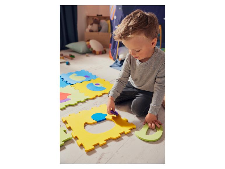 Een jongetje speelt met kleurrijke schuimmatten en puzzelstukken.
