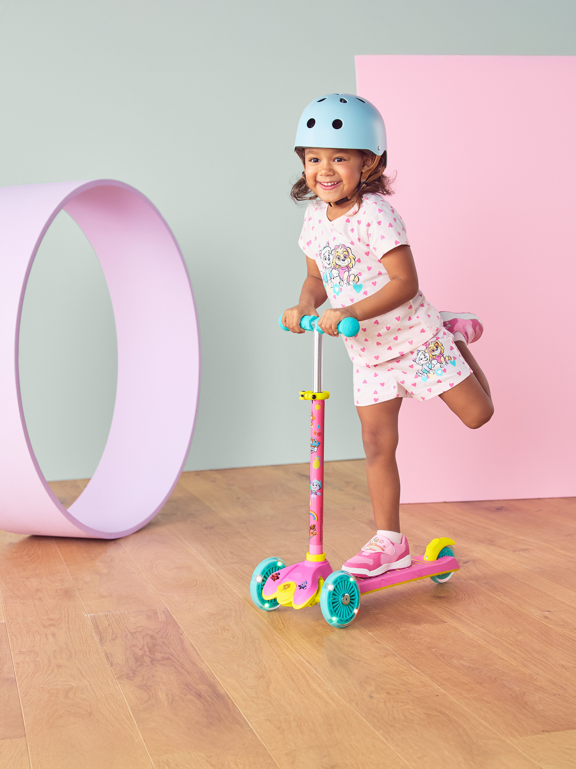 Meisje met helm en roze step met lichtgevende wielen, lachend.