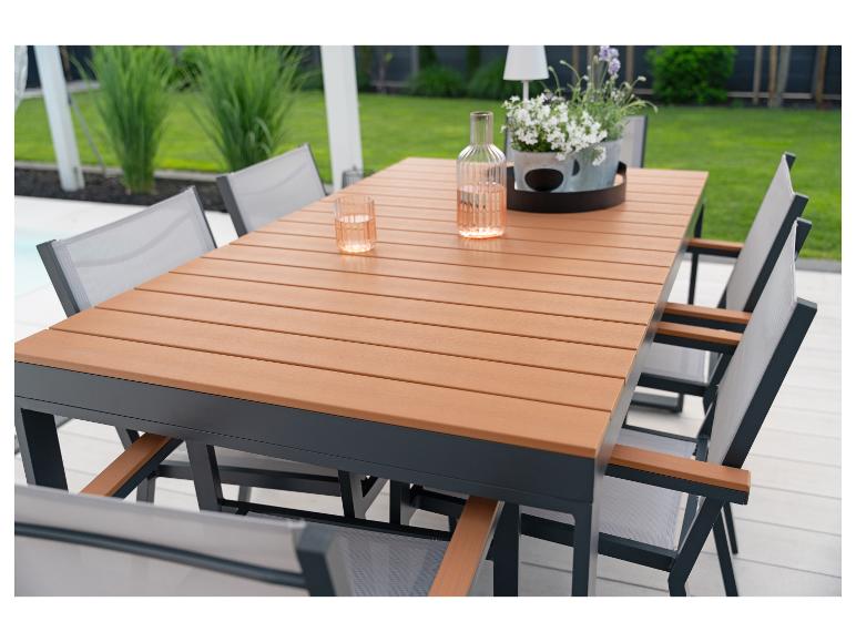 Buiten eethoek met houten tafel en grijze stoelen op een terras, met groen op de achtergrond.