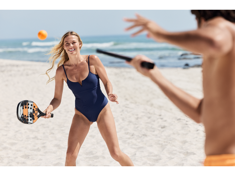 Vrouw in badpak speelt strandtennis met racket en bal op het strand.