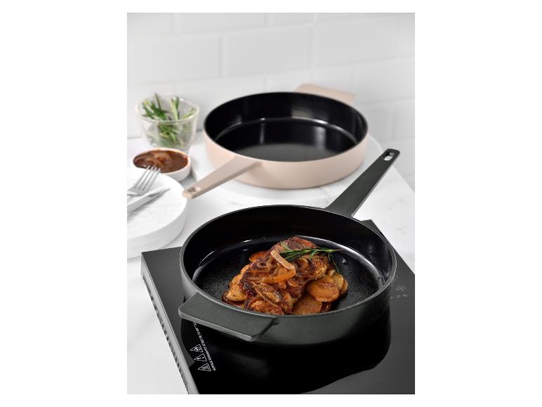 Koekenpan met aardappelen en gekarameliseerde uien op een inductiekookplaat, met een pan op de achtergrond.