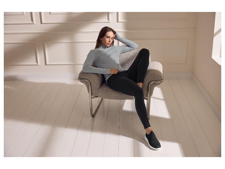 Vrouw in grijze coltrui en zwarte legging zittend in een fauteuil.