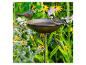 Vogelbad met metalen vogelbeeldje en levende koolmees, omringd door bloeiende bloemen.