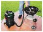 Aszuiger reinigt barbecue op terras, met groen gazon op de achtergrond.