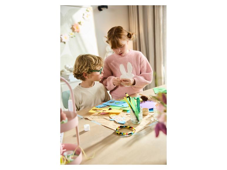 Twee kinderen maken paasdecoraties aan een tafel vol knutselspullen.