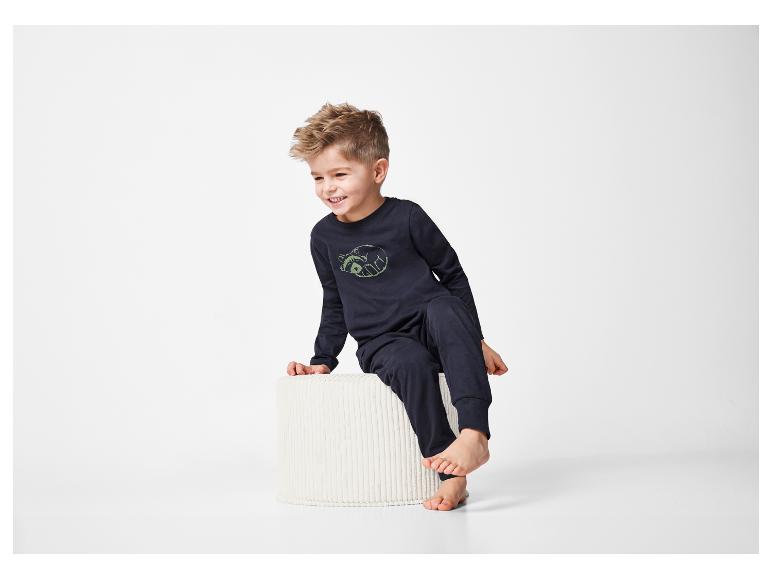 Een peuter in een donkerblauwe pyjama zit op een witte kruk.