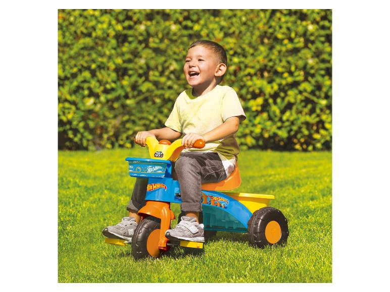 Een kind rijdt op een Hot Wheels driewieler in de tuin.