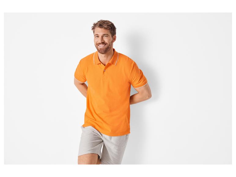 Lachende man in een oranje polo shirt en grijze shorts.