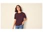 Vrouw in bordeauxrood T-shirt en jeans, met hand in zak.