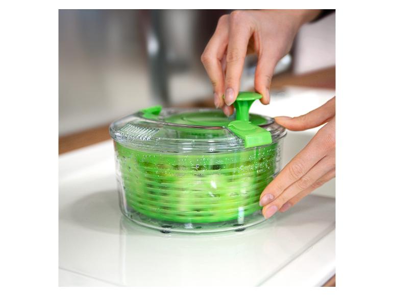 Handen gebruiken een groene slacentrifuge om sla te drogen.