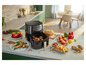 Een Philips Airfryer met gebakken kip, frietjes, muffins en groenten.