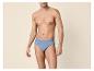 Man in blauwe katoenen slips, poserend tegen een beige achtergrond.