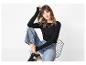 Vrouw in zwarte top met lange mouwen, wijde jeans en sneakers zittend op een stoel.