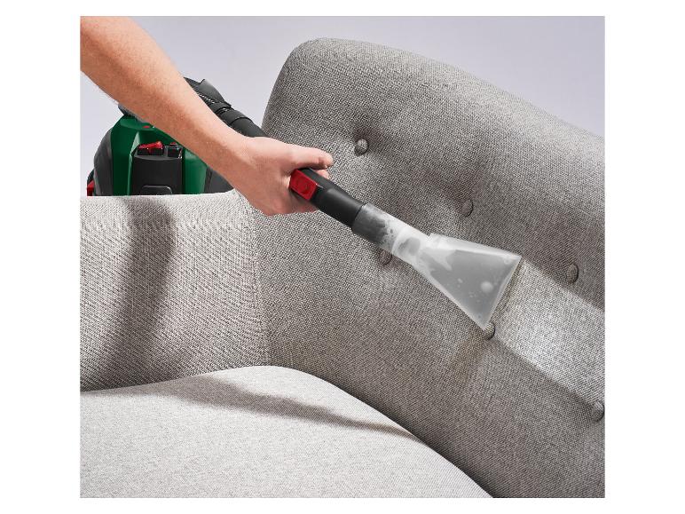 Hand reinigt een grijze stoffen bank met een bekledingreinigingstool.