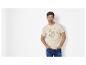 Man in een lichtbeige T-shirt met schildpadprint en tekst, blauwe jeans