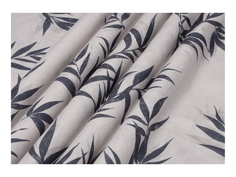 Witte stof met donkergrijs bamboebladpatroon, geplooid.