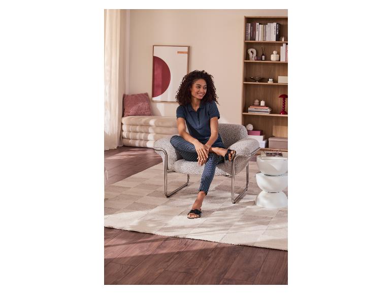 Vrouw zit in een fauteuil met gestreepte broek en poloshirt, in een gezellige woonkamer.