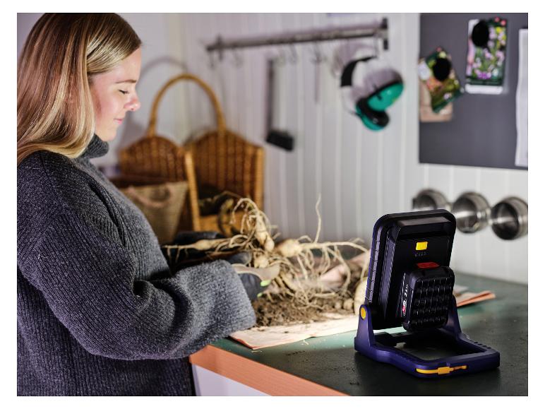 Vrouw plant planten met een LIVARNO® 18 V werklamp »BWL2400 P4A« die het werkgebied verlicht.