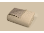 Gevouwen beige gewatteerde deken met een grijsbruine binnenkant en ruitvormige stiksels.