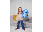 Lachend meisje met een blauw pluchen speelgoed, staand in een woonkamer.