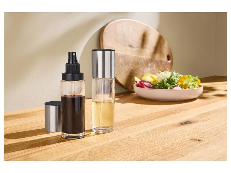 Olie- en azijnsprayflessen op een houten plank met een saladekom op de achtergrond.