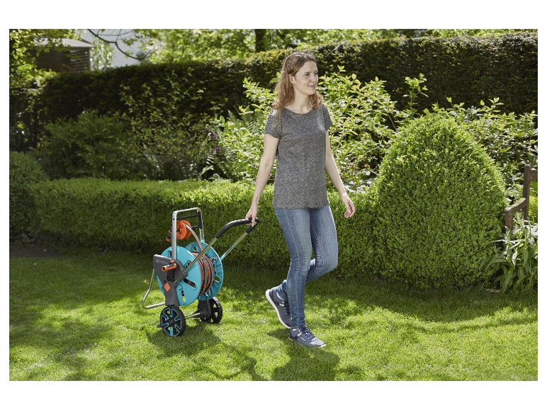 Een vrouw loopt met een Gardena tuinslangwagen over het gazon.