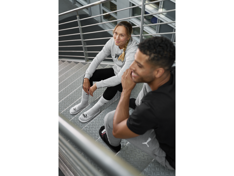 Twee mensen in PUMA-kleding zitten op een trap, de vrouw draagt een grijze hoodie en witte slippers.
