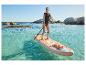 Vrouw in zwemvest op paddleboard in helder water met rotsen op de achtergrond.