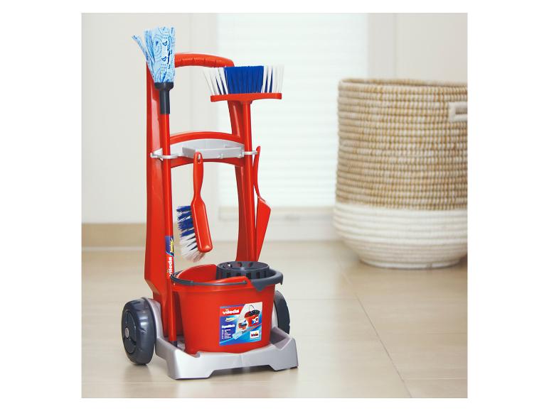 Rode Vileda Junior schoonmaakwagen met accessoires, naast een gevlochten mand.