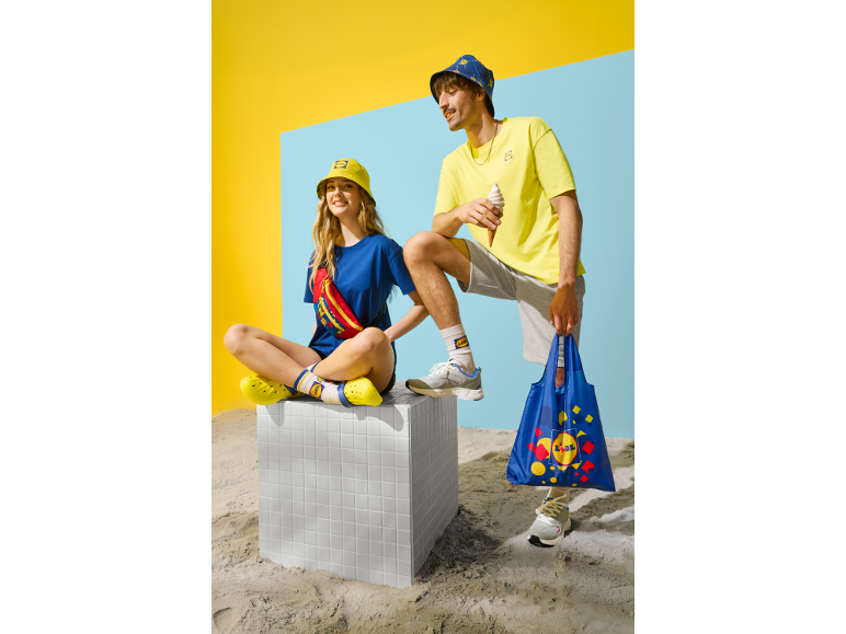 Twee mensen in casual zomerkleding, met bucket hats, T-shirts en boodschappentassen.
