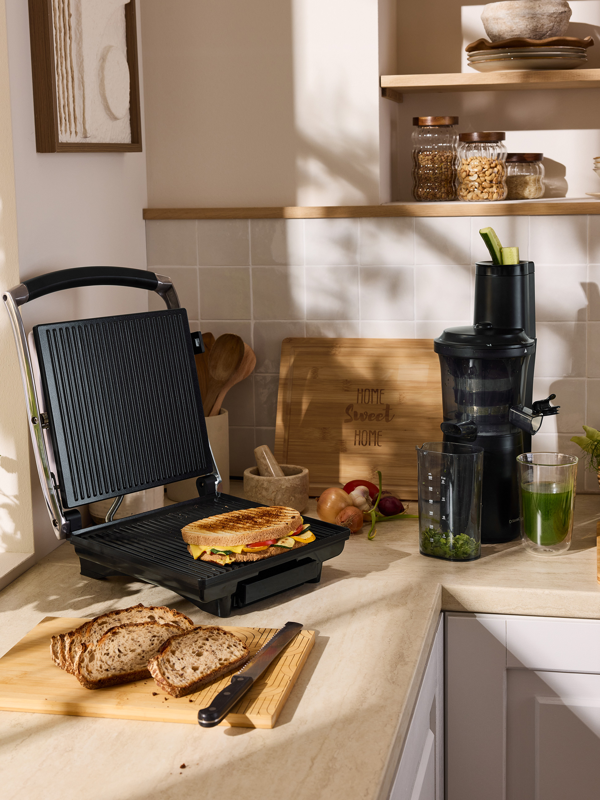 Een gegrilde sandwich op een tosti-ijzer, gesneden brood en een sapcentrifuge op een aanrecht.