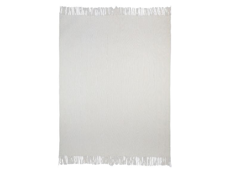 Een crèmekleurig gebreid deken met franjes.
