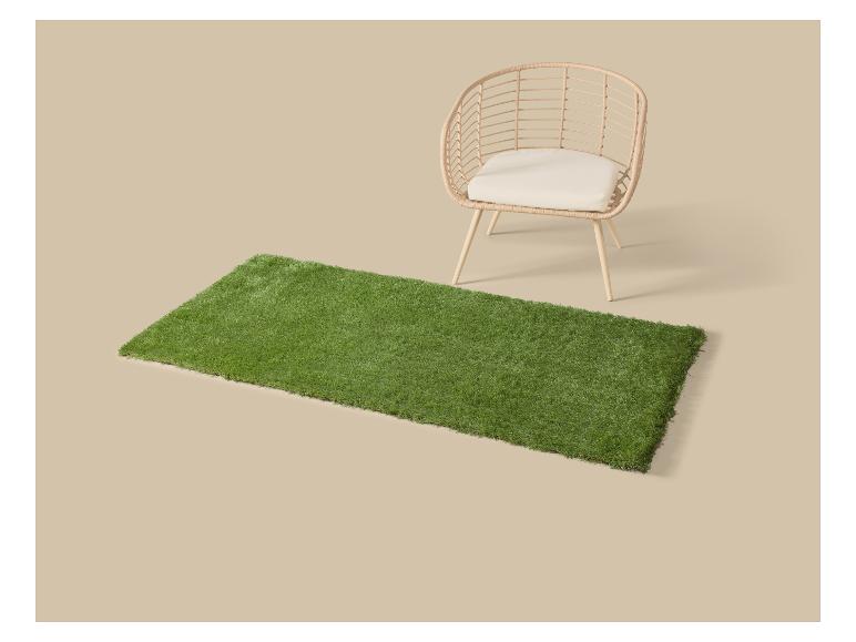 Groen kunstgras tapijt met een rieten stoel met kussen.
