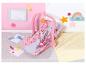 BABY born poppenautostoel in roze met bedrukte stof, omringd door kindertekeningen.