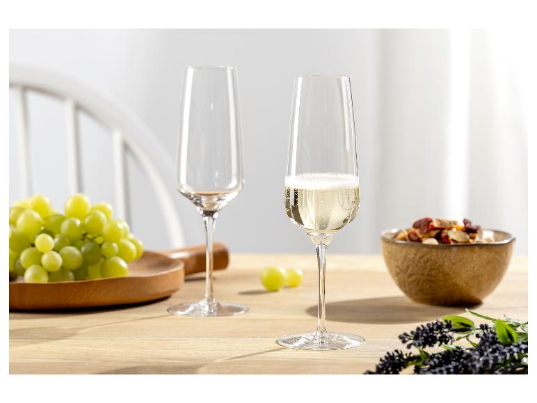 Twee champagneglazen, één gevuld met mousserende wijn, met druiven en noten op tafel.